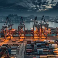 Пристанищни кранове товарят контейнерен кораб при здрач